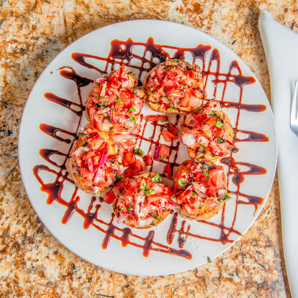 Six bruschetta pieces topped with diced tomatoes, onions, and herbs, drizzled with balsamic glaze.