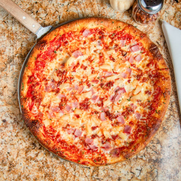 Mama Mia's Hawaiian pizza with ham, pineapple, and bacon on a pizza peel.