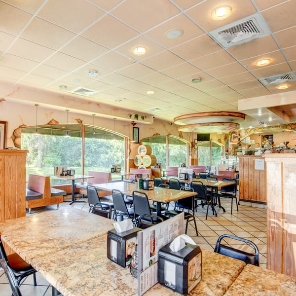 Bright, empty dining room at Mama Mia's Pizzeria with booth seating, tables, and large windows overlooking trees.