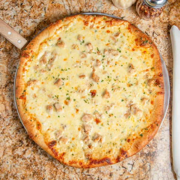 Mama Mia's white pizza with chicken and herbs on a pizza peel, with chili flakes and garlic.