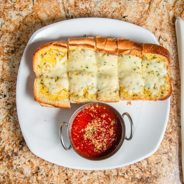 Cheesy garlic bread, sliced into pieces, with a side of marinara sauce on a white plate.
