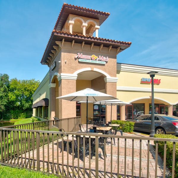 Exterior of Mama Mia's Pizzeria with outdoor seating under umbrellas, next to a pond.
