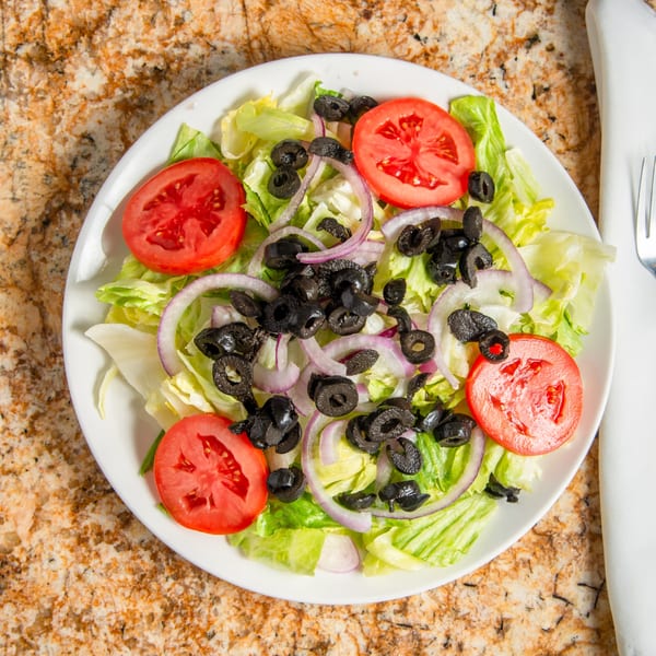 A fresh side salad with crisp lettuce, sliced tomatoes, red onions, and black olives.