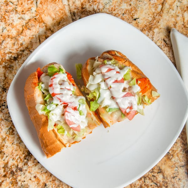 Two halves of a sub sandwich with lettuce, tomatoes, and white sauce on a white plate.