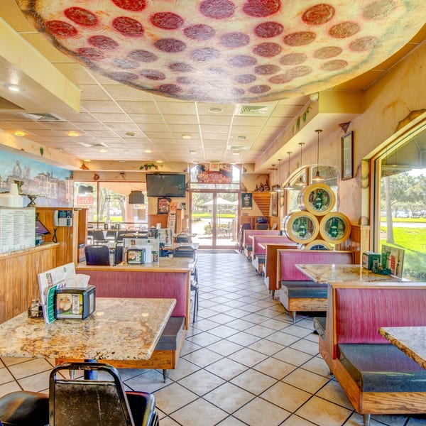 Interior of Mama Mia's Pizzeria with a large pizza slice mural on the ceiling and red booth seating.